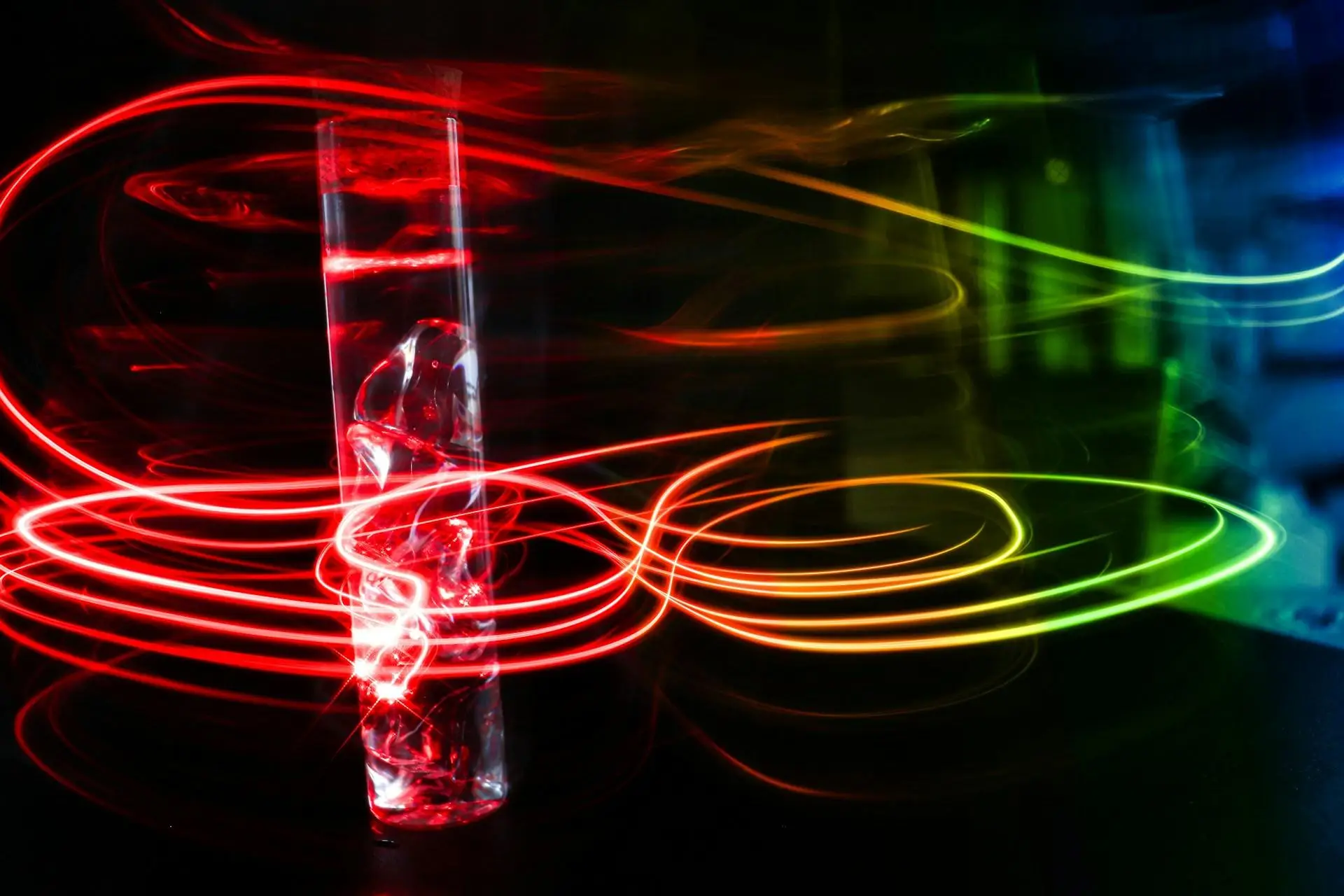 A glass surrounded by colorful light trails, predominantly red and yellow.