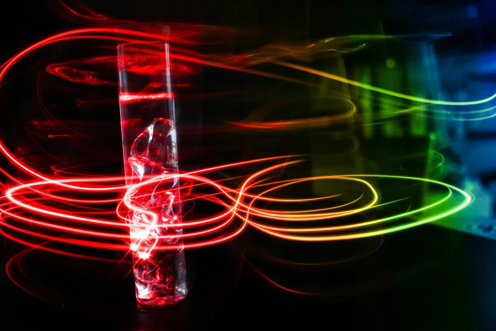 A glass surrounded by colorful light trails, predominantly red and yellow.